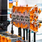 Black REVO-2 CMM Probe head measuring bright orange engine block for CMM inspection