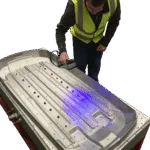 Man in high visibility vest scanning a large silver mould tool on-site.