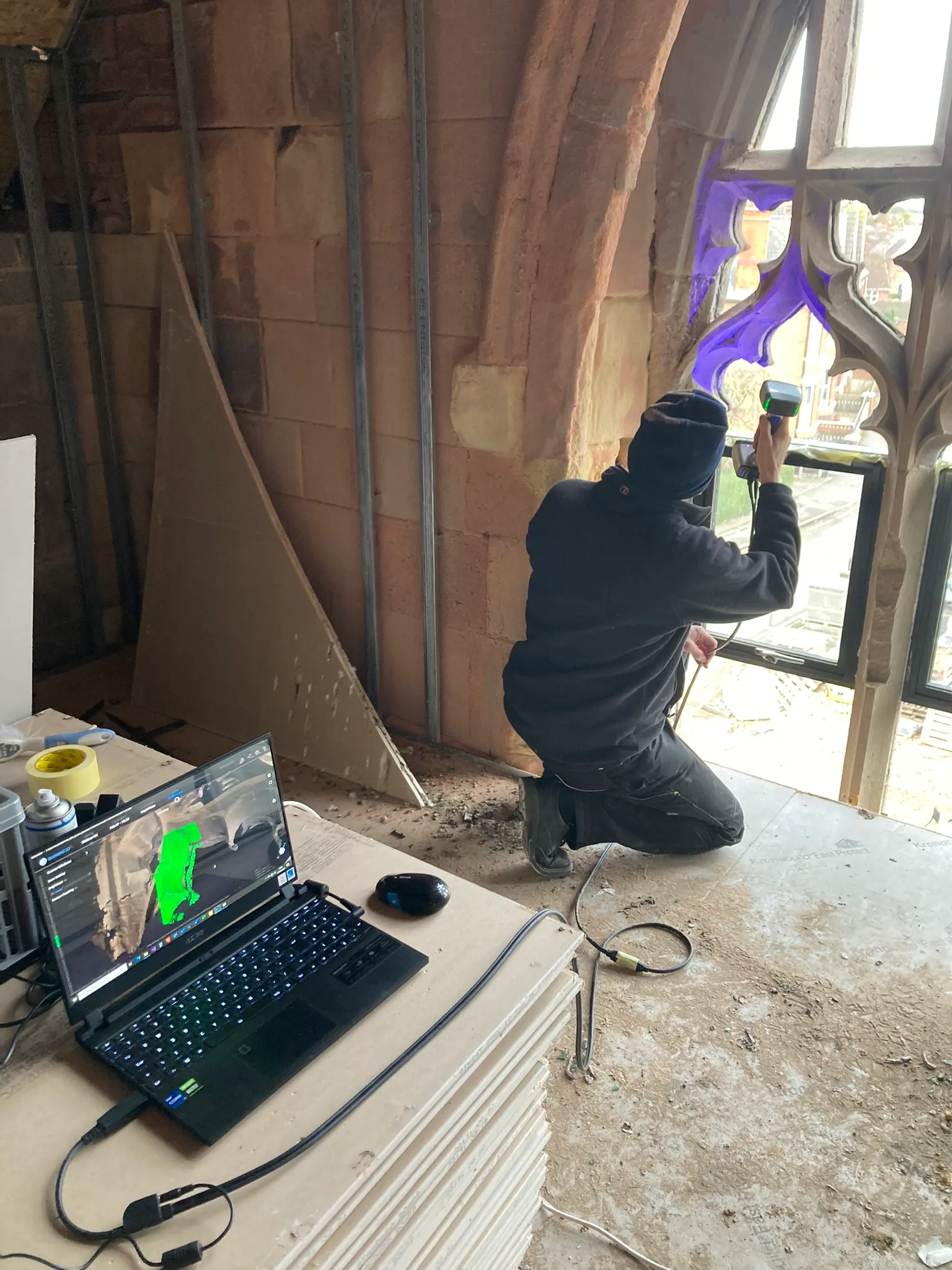 Adrian using handheld 3D scanner on church stonework, laptop shows scanned model in foreground.
