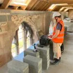 Person in full construction site PPE with laptop set upon breeze blocks reviewing 3D scan data.