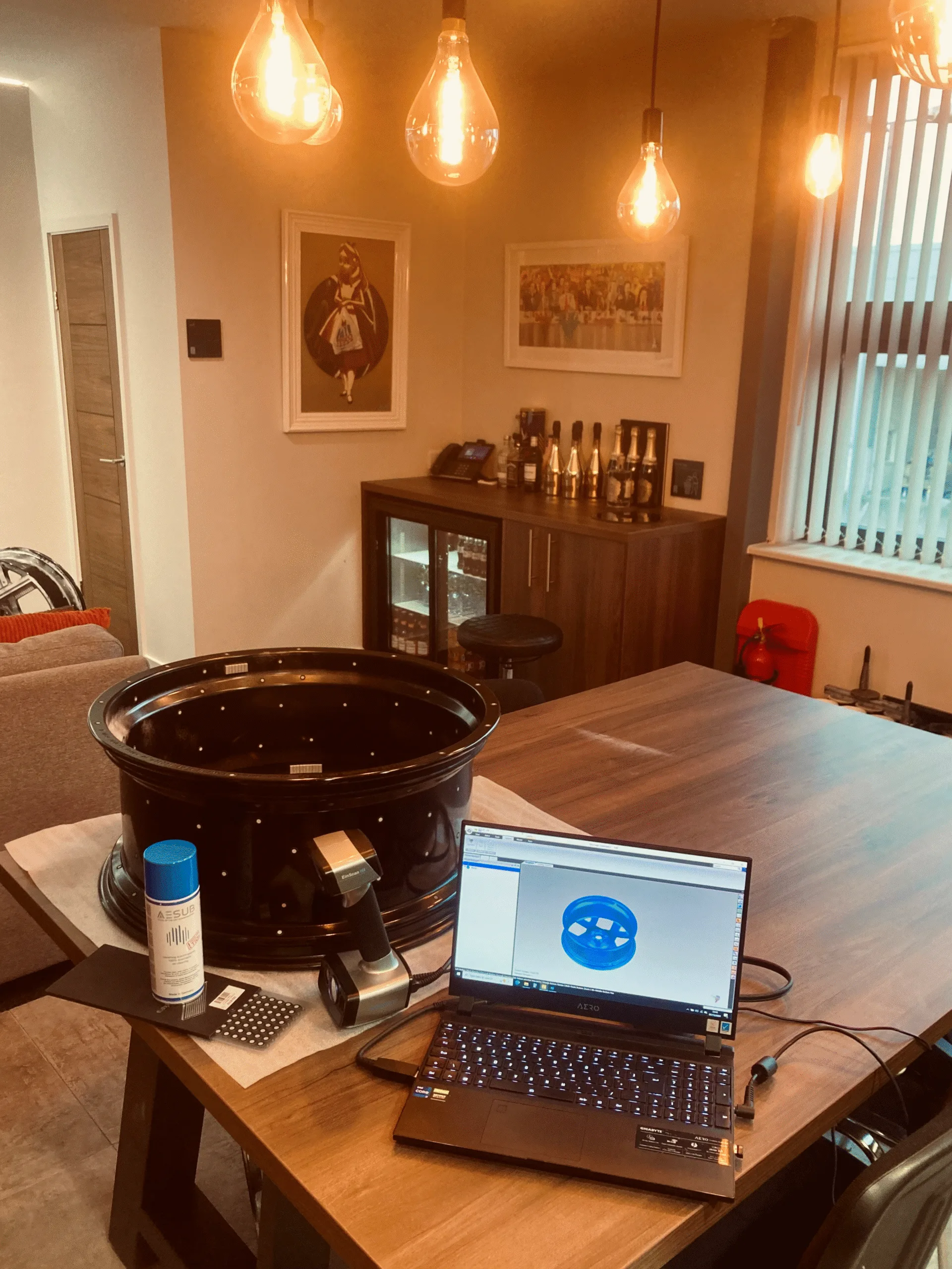 3D scanning setup on table with black alloy wheel, handheld scanner, spray, and laptop mesh.