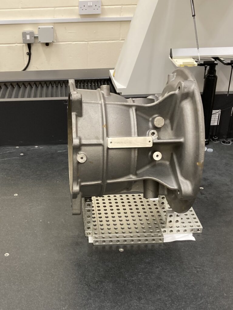A large silver casing on a metal fixturing plate, set on a granite CMM bed ready for inspection using our Metrology-as-a-Service model; a CMM probe is visible in the background.